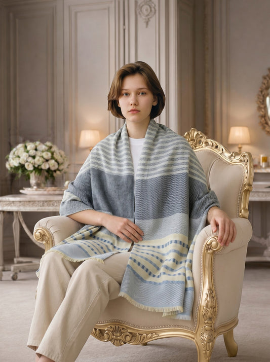 Noori Couture grey, white, and pale yellow striped herringbone cashmere scarf draped on a model sitting in an ornate chair.