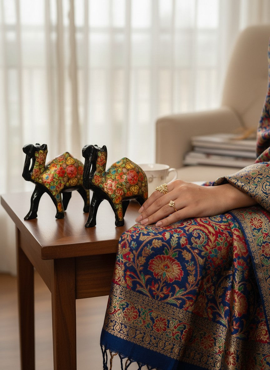 Noori Couture hand-painted black camel figurines adorned with vibrant floral patterns, displayed on a wooden table.
