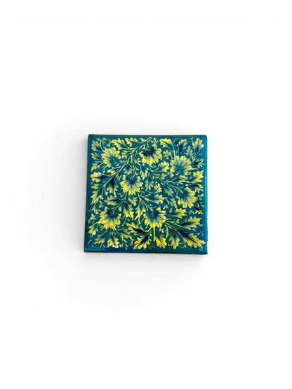 Noori Couture hand-painted papier-mâché square coaster with intricate yellow floral design on teal background.