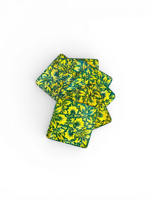 Noori Couture hand-painted papier-mâché coasters with intricate yellow floral design on a teal background.