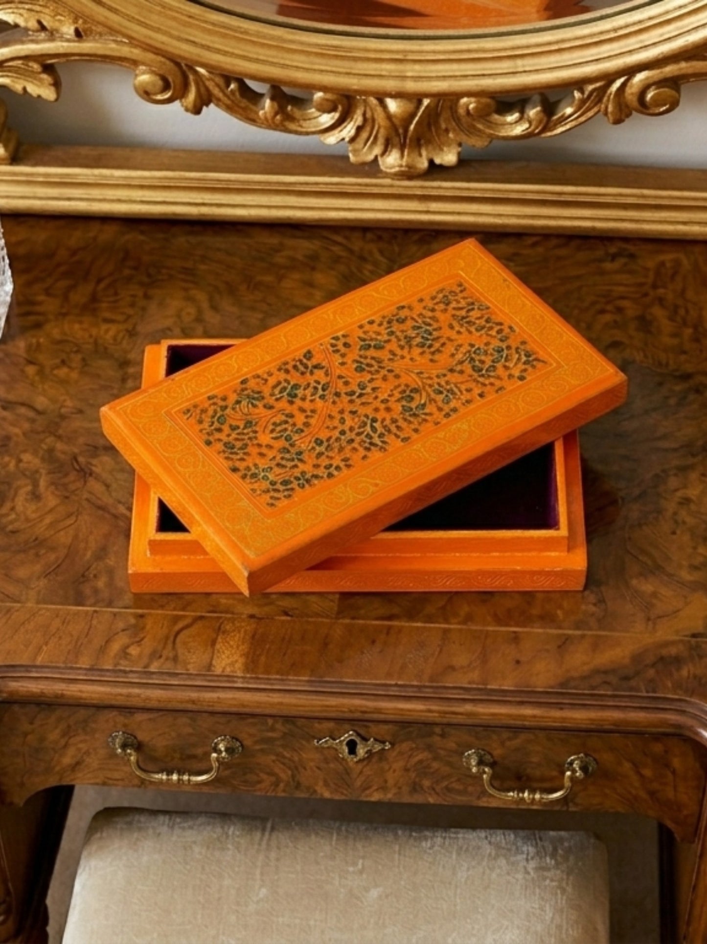 Noori Couture orange papier-mâché keepsake box with hand-painted floral details, open on a wooden vanity.
