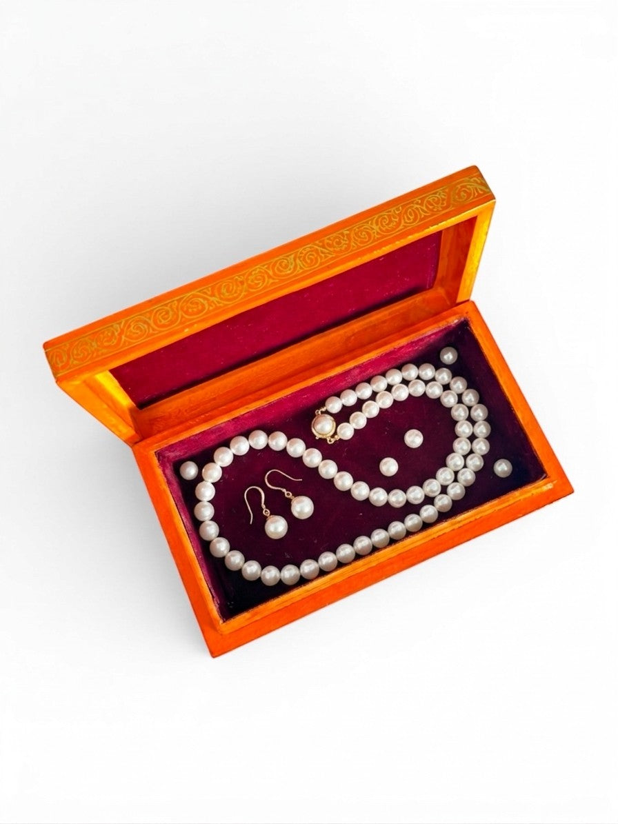 Noori Couture orange papier-mâché keepsake box with red velvet lining, holding a pearl necklace and earrings.