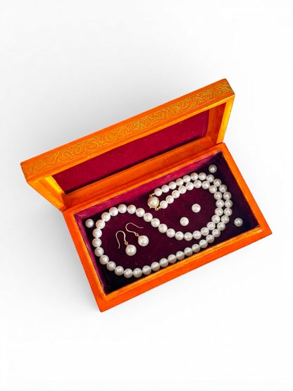 Noori Couture orange papier-mâché keepsake box with red velvet lining, holding a pearl necklace and earrings.