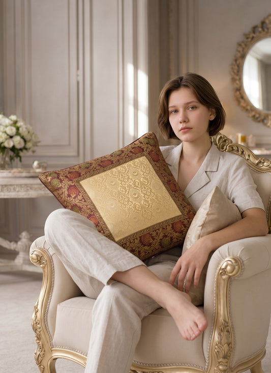 Noori Couture Royal Cushion Cover in gold brocade with intricate zari detailing and floral motifs in burgundy and green.