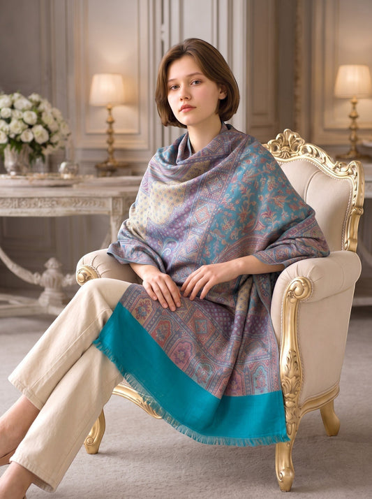 Noori Couture pashmina shawl with teal and violet paisley patterns draped over a woman sitting in a classic armchair.